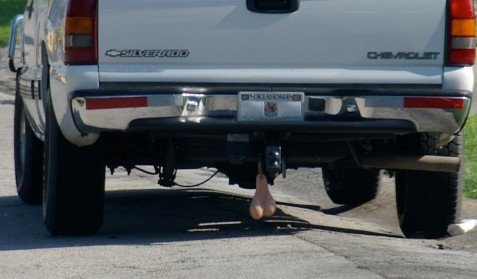 A photograph of the rear end of a pickup truck bumper, with fake rubber bull testicles hanging from the tow hitch.  Seriously.